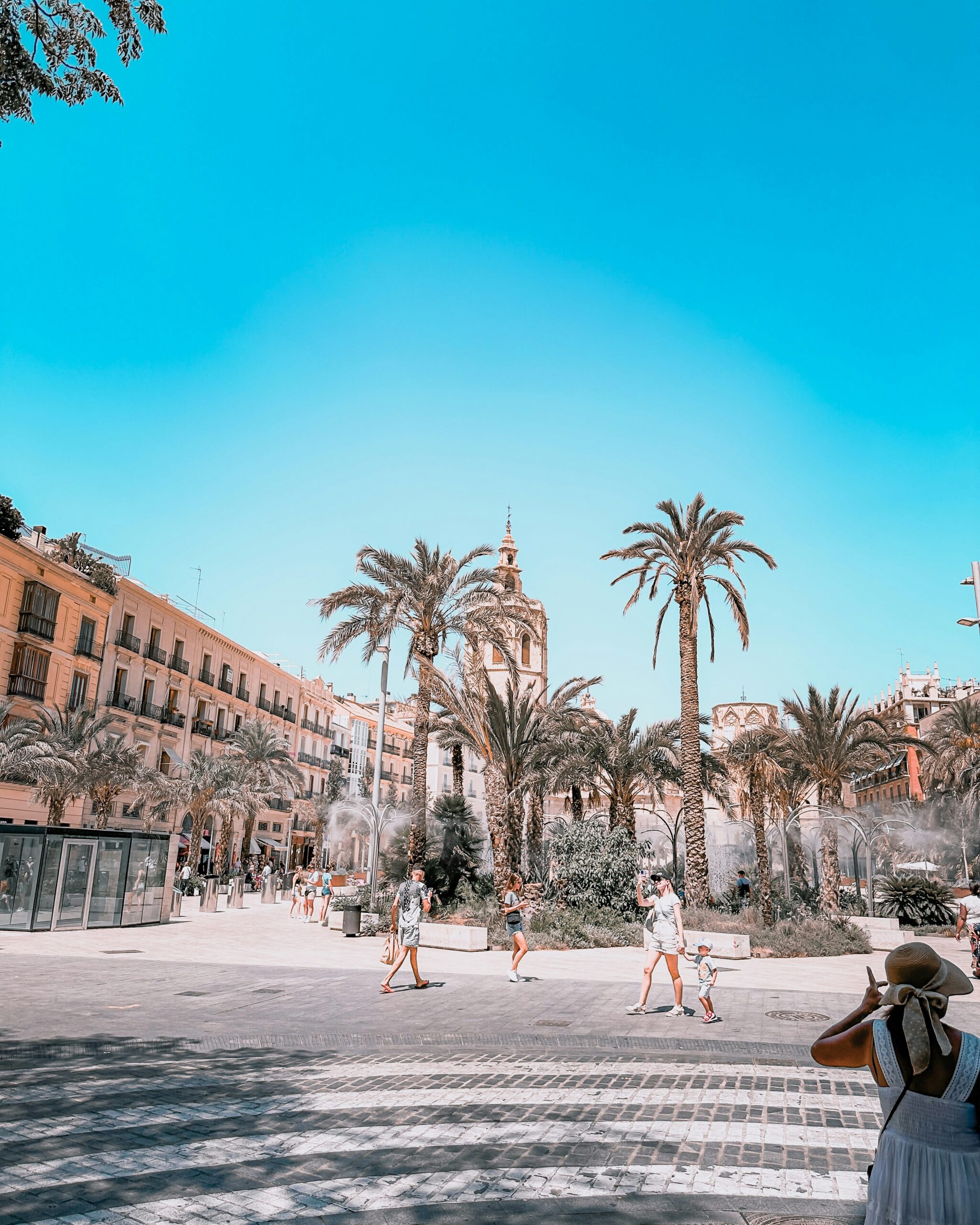 People walking in a sunny Valencia plaza with palm trees before relocating to Spain
